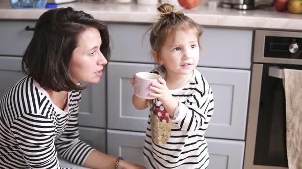 Mother Gives Her Daughter a Cup of Water Little Girl Drinks Mom is Smiling on the Kitchen