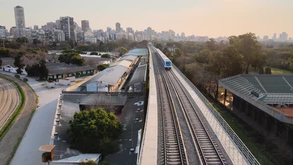 Aerial view of passing Mitre Line Train with skyline of Buenos Aires in background during sunset