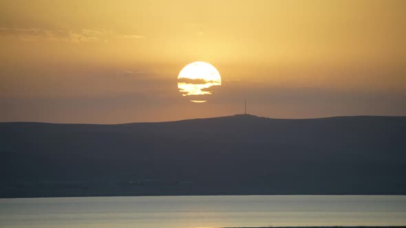 8K Sunset From Behind the Hills at the Edge of the Body of Water