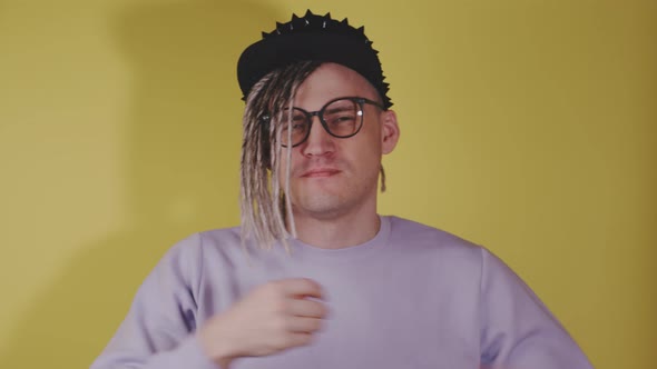 Young handsome man with dreadlocks in black cap, glasses preening himself in front of camera