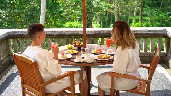 Young Couple Enjoying The Breakfast On The Terrace With The Jungle View In Bali, Indonesia