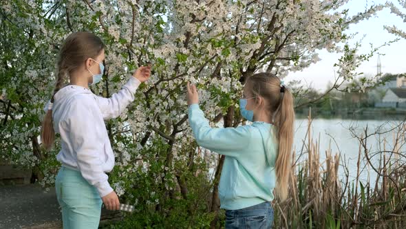 Allergy pills. Two little girls at the flowering tree in medical masks.