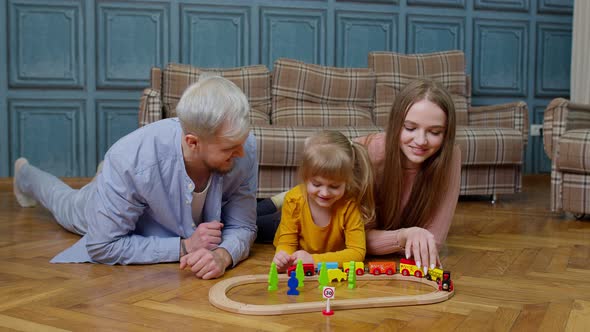 Family of Mother Father with Daughter Child Girl Riding Toy Train on Wooden Railway at Home Room