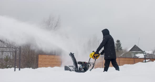 Man Cleans Snow With Snowplough at House Courtyard