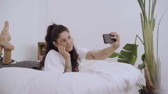 Young Woman Lying on Bed Taking Selfie