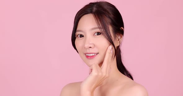 Young Beautiful Asian woman touch her face gently with fingertips on pink background.