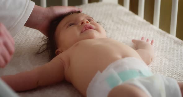 Caring Mother Stroking a Newborn Baby in a Diaper Lying on Her Back in Crib