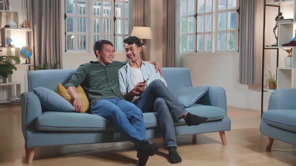 Happy Asian Gay Couple Watching Tv While Sitting On A Couch In Apartment, Watching Funny Videos