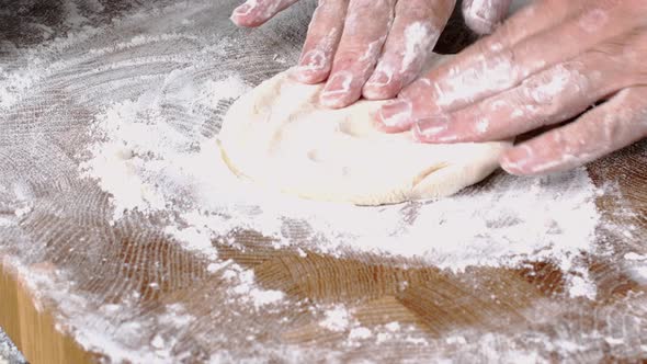 Human hands roll out fresh dough for make bread or pizza on kitchen board for baking.