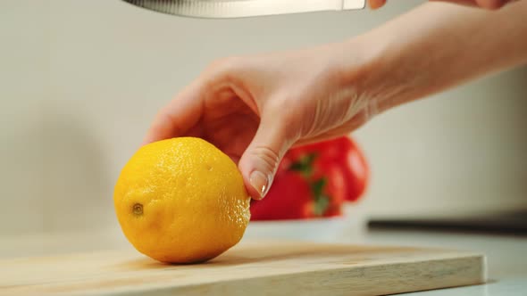 Hands with Knife Cutting Lemon on the Kitchen Board