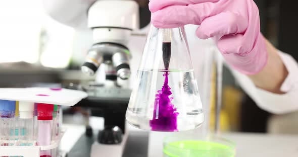 Scientist Chemist Dripping Pink Liquid Into Glass Flask with Water in Laboratory Closeup Movie Slow