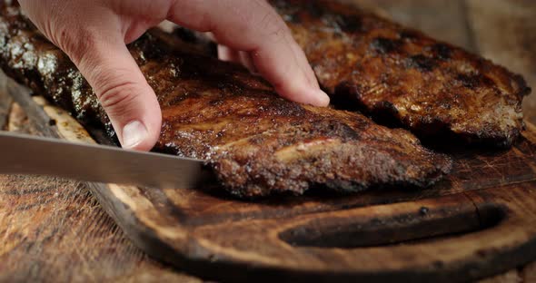 Men's Hands with a Knife Cut Fried Ribs on the Grill
