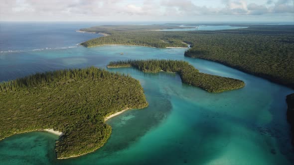 Slow flyover above small, forested sunlit islands in Oro Bay, Isle of Pines.