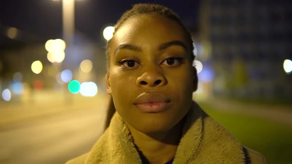 A Young Black Woman Looks Seriously at the Camera in a Street in an Urban Area at Night  Closeup