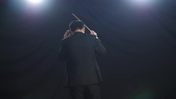 Back View Of Asian Conductor Man Holding A Baton And Showing Gesture In The Black Studio