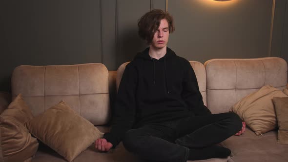 Young Handsome Man Doing Breathing Exercise While Sitting on Sofa at Home