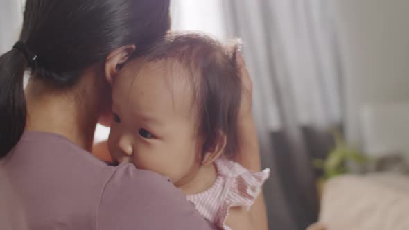 Asian Mother Cuddling Baby Daughter at Home