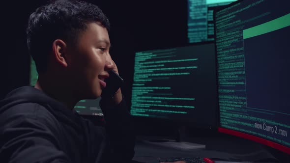 Asian Boy Hacker Using Computer Hacking And Talking On Phone