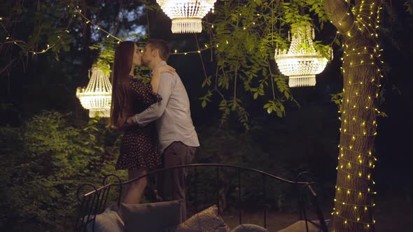 Happy Husband Kissing and Hugging Loving Wife with Romantic Lights Around. Portrait of Caucasian