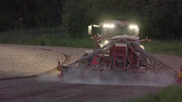 Tractor with lights on sowing seeds at dusk in Hedemora, Sweden, wide shot