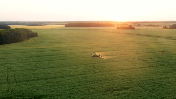 Aerial Tractor Trailer Sprays Mineral Fertilizer On Agricultural Field At Sunset