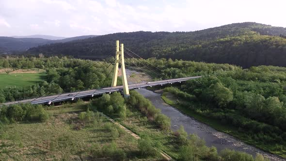 huge yellow bridge in the forest, moving cars and flowing river - aerial shot