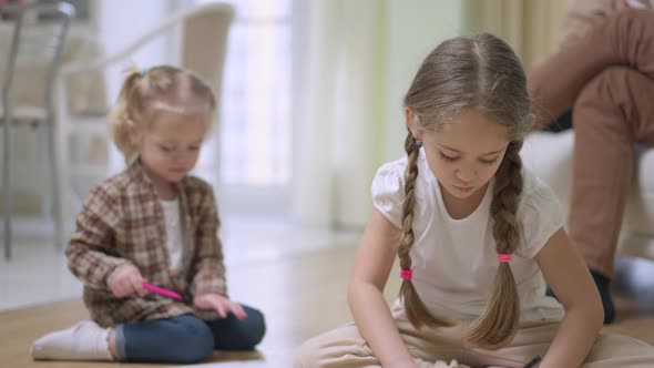 Portrait of Concentrated Charming Caucasian Girl with Pigtails Painting Sitting on Floor with