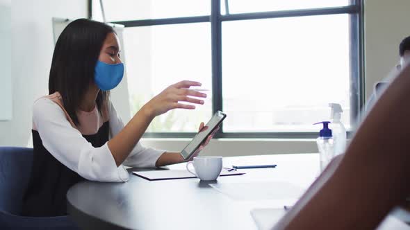 Asian woman wearing face mask using digital tablet while sitting on her desk at modern office