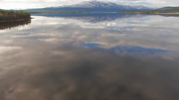 Swedish Alpine Forest Lake Reflecting Snowcapped Mountains. Camera Tilt Up From Water To Reveal Lake