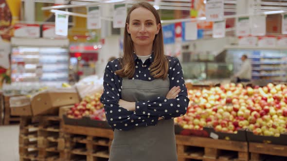 Portrait of a Female Worker in an Apron Against a Background of Fruits a Young Woman Crosses Her