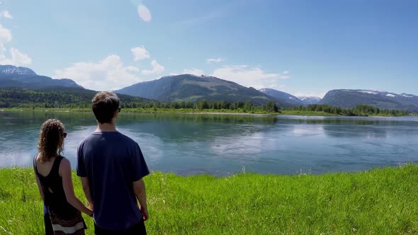 Couple watching beautiful lake surrounded by mountain range 4k