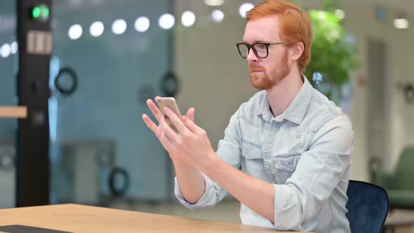 Serious Young Redhead Man Using Smartphone in Office