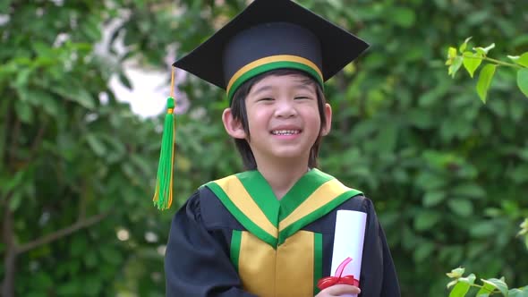 Happy Asian Child In Graduation Gowns Holding A Certificate