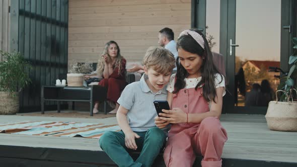 Siblings Using Smartphone on Porch