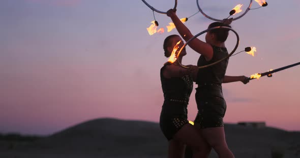 Women with Fire at Sunset on the Sand Dance and Show Tricks Against the Beautiful Sky in Slow Motion