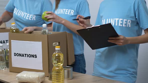 Volunteers Putting Groceries in Boxes While Supervisor Checking List, Donations