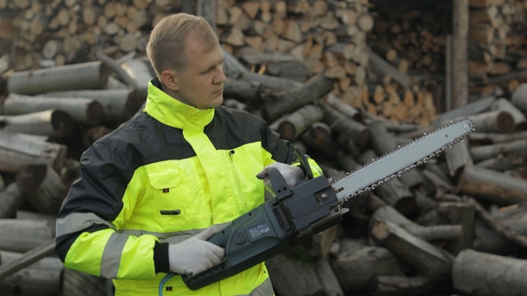 Lumberjack in Reflective Jacket. Man Woodcutter with Electric Chainsaw, Sawn Logs, Firewood, Sawmill