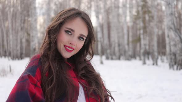 Young Woman with Wavy Hair Standing and Touching Face in Winter Forest