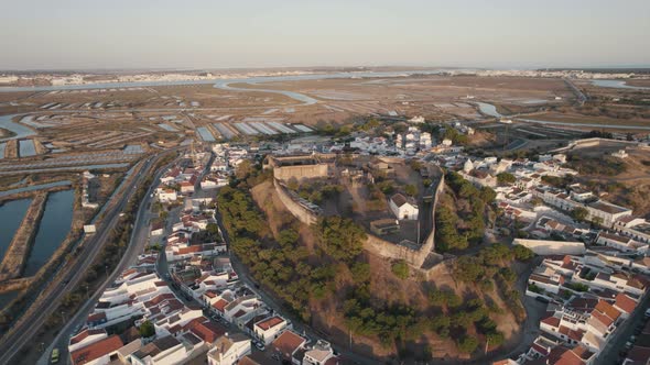 Aerial drone flying over hilltop Castelo de Castro Marim Castle, village settlements and salt flats.