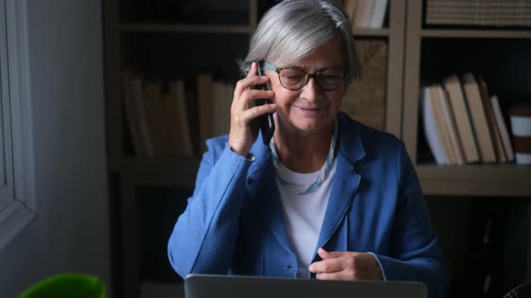 Senior woman talking on the phone while working on laptop