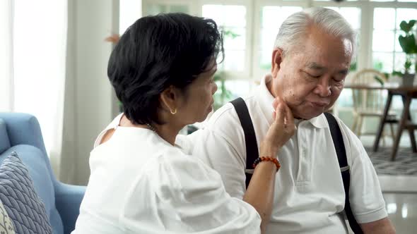 Unhappy Retired Asian Senior Couple Sit on Sofa While Elderly Wife Comforting a Sad Husband at Home