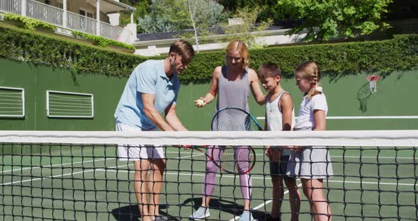 Caucasian father and mother teaching their kids to play tennis at tennis court on a bright sunny day