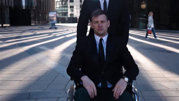 Businessman Tote His Cripple Colleague in Wheelchair Outdoor