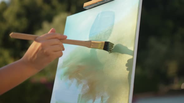 Closeup Female Hand Painting on Canvas with Silhouette Shadow of Wine Glass Reflecting in Sunshine