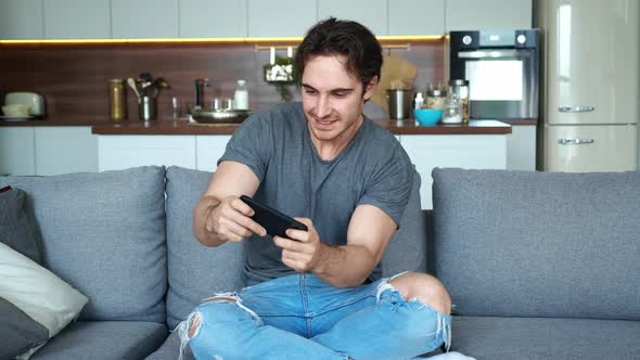 Young Man Playing on His Smartphone Exciting Mobile Application Winning a Racing Game Clenching Fist