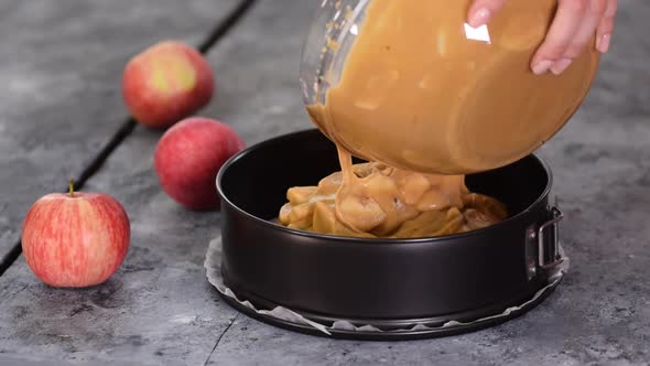 Female chef hands pouring batter into baking dish for apple pie.