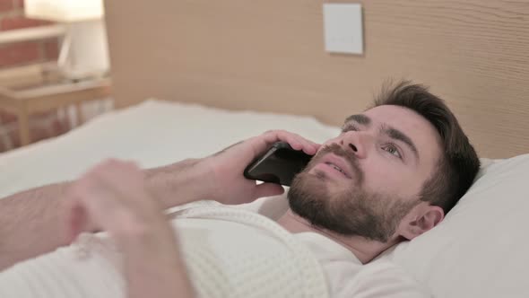 Young Man Talking on Smartphone in Bed 