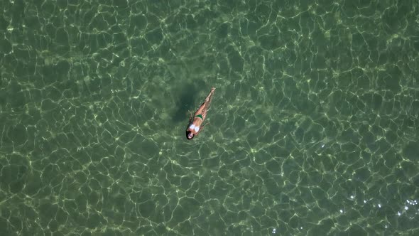 A young woman floats and enjoys the waters of the Aegean Sea near Paros island in Greece; medium sho