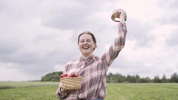 Happy Young Woman is Standing in Green Field and Waving Her Cap in the Air