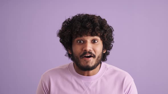 Surprised curly-haired Indian man looking at the camera